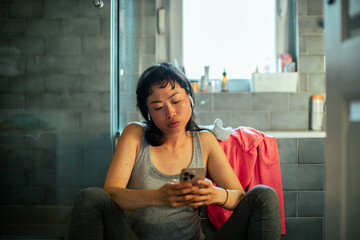 Young asian woman using a smartphone in the bathroom after exercising and working out in the gym