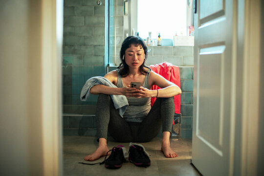 Young asian woman using a smartphone in the bathroom after exercising and working out in the gym