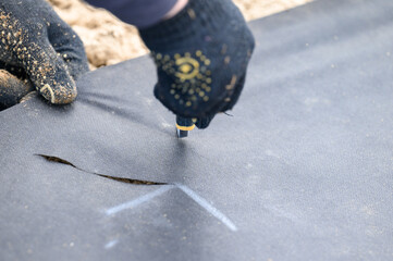 A man cuts a black agricultural fiber along the label