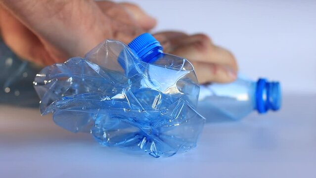 Man's hands crushing a plastic bottle in the background, a crushed bottle in the foreground, recyclable plastic bottle, reduce size, recycling.