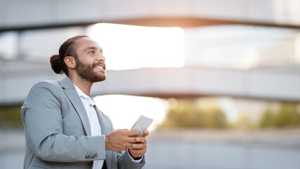 Smiling Handsome Young Businessman With Smartphone In Hands Standing Outdoors