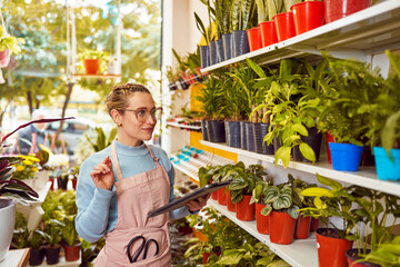 portrait caucasian female employee holding a digital tablet taking inventory looking inside plant store