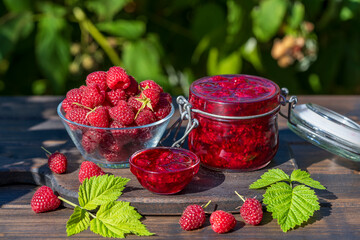 Red raspberry jam and fresh raspberry on a rustic wooden table outdoors near garden. Rustic style, closeup