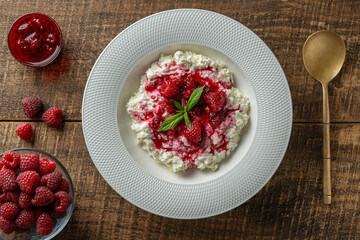 Fresh white cottage cheese with sour cream and red raspberry jam on wooden background, closeup, top view