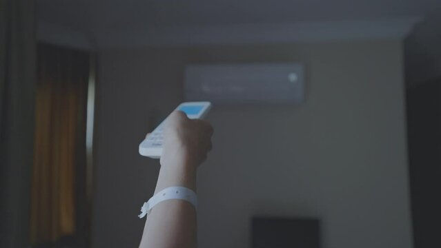 Female hand holding remote control aimed at air conditioner mounted in hotel room wall