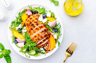 Gourmet salad with grilled peaches, chicken breast, blueberries, red onion, feta cheese, basil and mixed herbs, white table background, top view