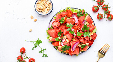 Exotic vegan salad with sweet watermelon, cherry tomatoes, red onion, peanuts and parsley, white table background, top view