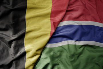 big waving national colorful flag of belgium and national flag of gambia .