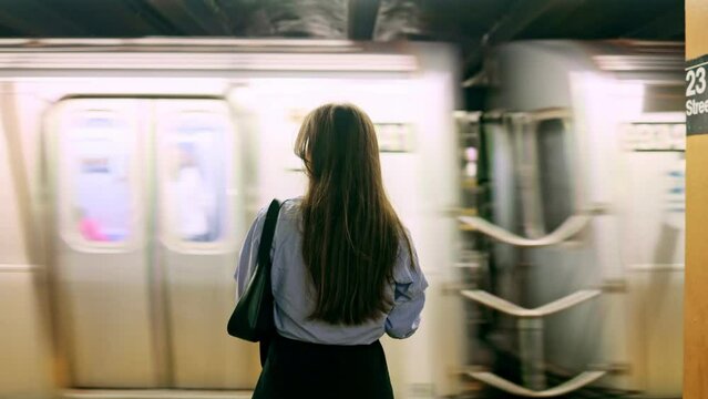Young girl in the New York subway. Brunette woman standing on railway station, waiting for train. Girl in underground at evening looks on fast trams. Metropolis, freedom and active lifestyle concept.
