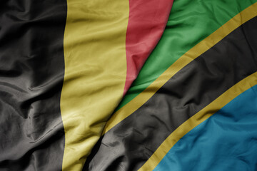 big waving national colorful flag of belgium and national flag of tanzania .