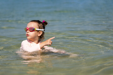 Portrait of young girl kid wearing goggles and sun protection shirt in the sea.