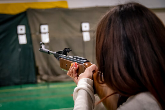 Brown-haired girl shooting at a target with an air rifle
