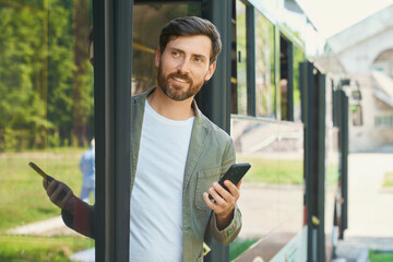 Smiling handsome businessman with cellphone getting off public transport. Front view of busy...