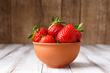 Large berries of organic strawberries in a clay ceramic bowl on a wooden background.