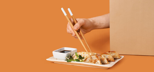Female hand with chopsticks, Chinese dumplings, tofu cheese and soy sauce on orange background