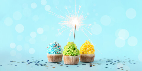 Tasty birthday cupcakes with sparkler on light blue background