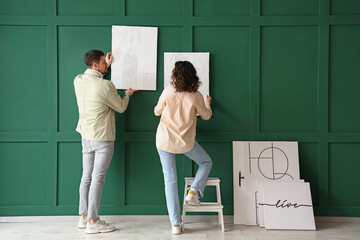 Young couple hanging paintings on green wall at home