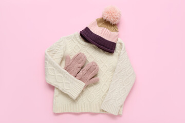 Stylish children's sweater, warm hat and mittens on pink background