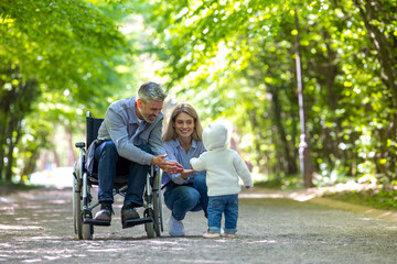 Father in wheelchair and mother with baby playing in park.