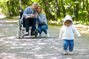 Fototapeta premium Father in wheelchair and mother with baby playing in park.