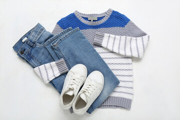 Stylish children's sweater, jeans and shoes on light background