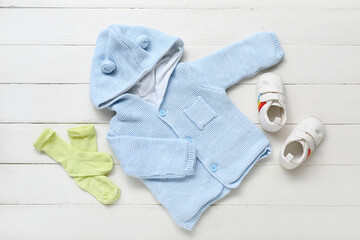 Knitted baby sweater, socks and booties on white wooden background