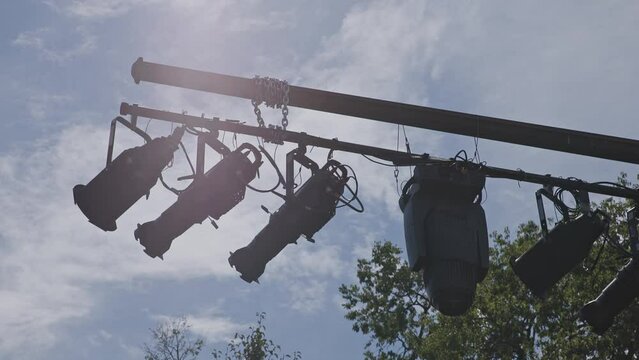 Handheld slow motion view of theatrical lightings, leko heads, and silhouettes of stage lights during an afternoon at public outdoor theatre with sun and clouds in the background