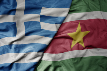 big waving national colorful flag of greece and national flag of suriname .