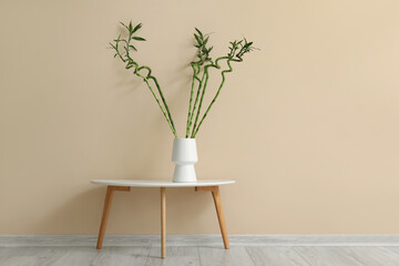 Vase with bamboo stems on table near color wall