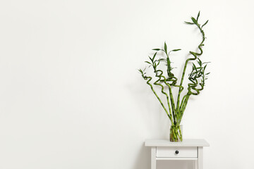 Vase with bamboo stems on table near light wall