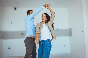 Happy Couple Dancing Together Out Of Happiness For Buying New Apartment. Young cheerful couple having fun while dancing during their home renovation process.