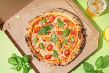 Carton box with tasty pizza Margarita and glass of beer on green background