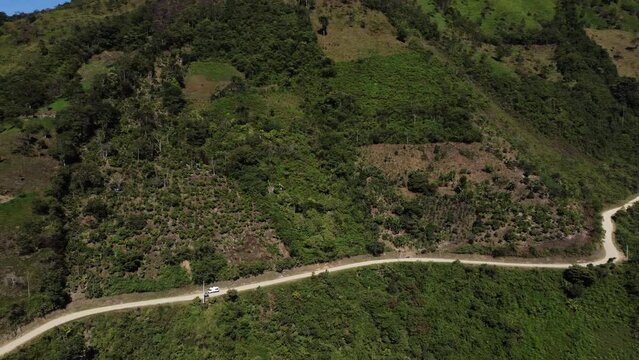  Camera following a small white van driving through green landscape on a thin winding gravel road