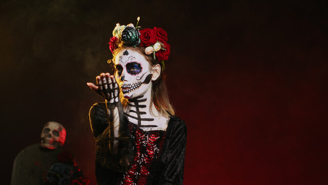 Creepy beautiful model sending air kisses on camera, wearing flowers crown and skull make up with kissy face. Looking like la cavalera catrina, being flirty on day of the dead. Handheld shot.