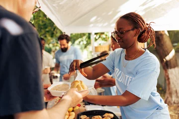  Detailed image of black woman at a food drive sharing free warm meals to poor caucasian homeless person. At local center group of volunteers feed and support the hungry and underprivileged. © DC Studio