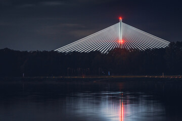 Wroclaw, Redzinski Bridge illuminated at night, the structure rises high above the trees on the banks of the Odra River. - obrazy, fototapety, plakaty