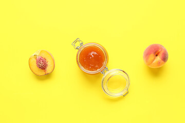 Glass jar of sweet peach jam and fresh fruits on yellow background