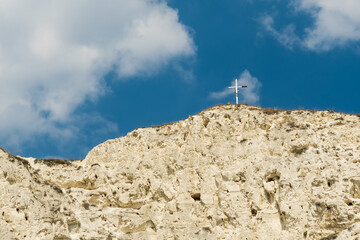 A Rocky Mountain Ridge Where a Cross Has Been Placed is Being Covered by Thick White Clouds on a Blue Sky Background