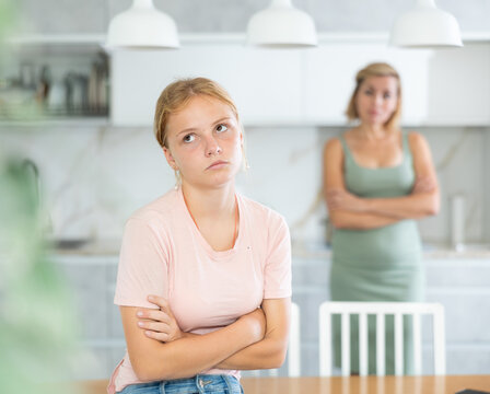 After conflict unpleasant conversation, mother and teenage daughter do not talk to each other. Woman and girl crossed arms and are standing apart from each other, mom is blurred and unrecognizable.