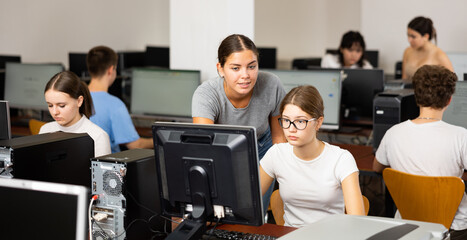 Schoolgirl using computer and teacher helping to him in classroom - obrazy, fototapety, plakaty