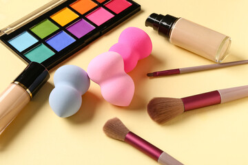 Set of makeup accessories, liquid foundation and eyeshadows on color background, closeup