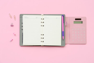 Composition with blank open notebook, calculator and paper clips on pink background