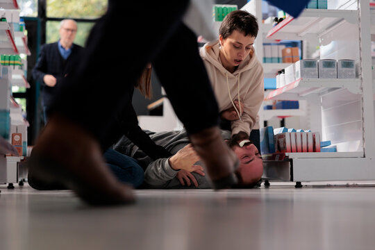 Pharmacy customers helping man managing epilepsy attack, rushing to give first aid. Young person lying on floor and suffering from forthy saliva and convulsion movements seizure symptoms