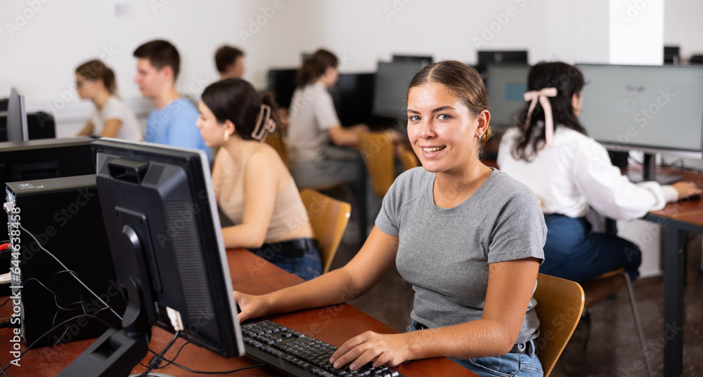 Poster excited female teenager learning computer science while she is using a pc in the computer classroom