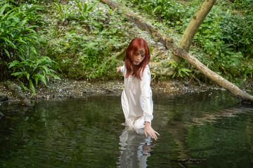 A young teenage girl in a white dress stands in a lake against a background of green foliage. day Ivan bathed.