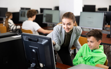 Female teacher and her student, young boy, looking at monitor of PC during computer science lesson.