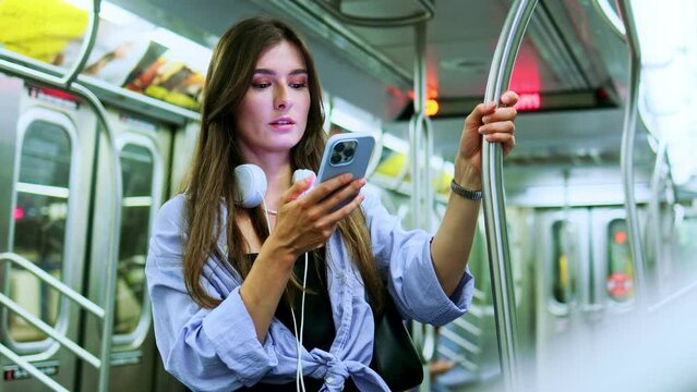 Beautiful adult female standing in half empty public transport holding handrail, enjoying traveling. Brunette young woman chatting, texting, using wi-fi internet while traveling in underground train.