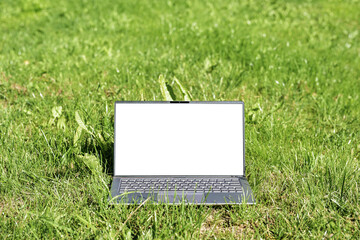 Laptop computer with white screen mock up in the grass on a meadow, green business concept, sustainable lifestyle and environmental protection, and resource conservation, copy space