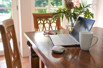 Laptop computer on a wooden dining table with coffee cup and flower bouquet in the living room, concept for home office working, copy space, selected focus