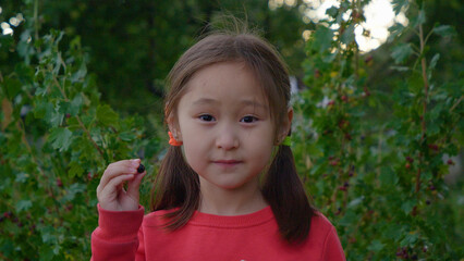 A cute girl picks up a fruit, points to the camera and eats